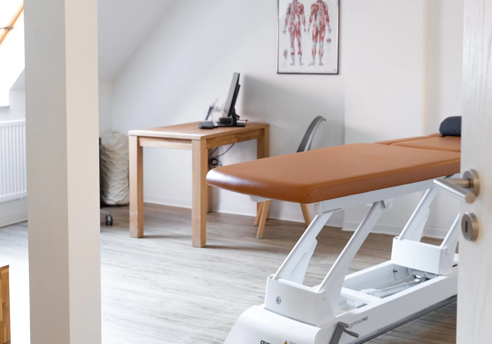 Behandlungsraum bei Fit im Norden mit Therapieliege und Muskelschautafel